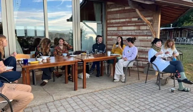 Une dizaine de personnes attablées en terrasse, tasses et assiettes sur les tables, grande baie vitrée derrière