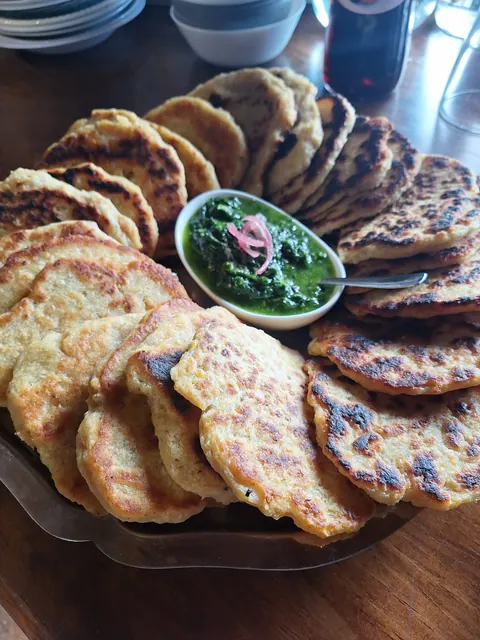 Plateau de galettes dorées autour d’un bol de sauce verte aux herbes