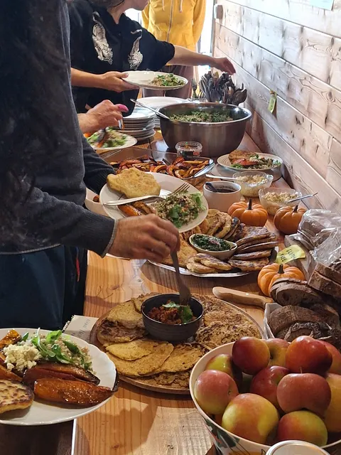 Plusieurs personnes se servent au buffet en bois, mains tendues vers les plats