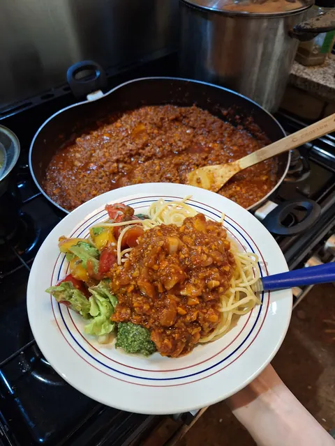 Assiette de spaghetti bolognaise au tofu devant la cocotte de sauce sur le feu