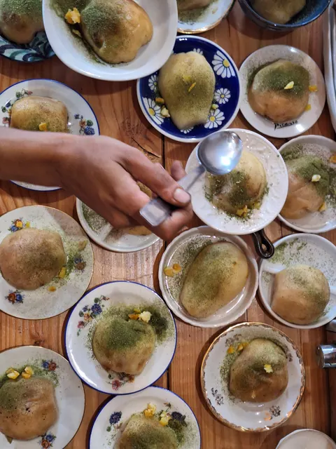 Une main sert du sirop sur des fruits pochés saupoudrés de poudre verte, assiettes fleuries