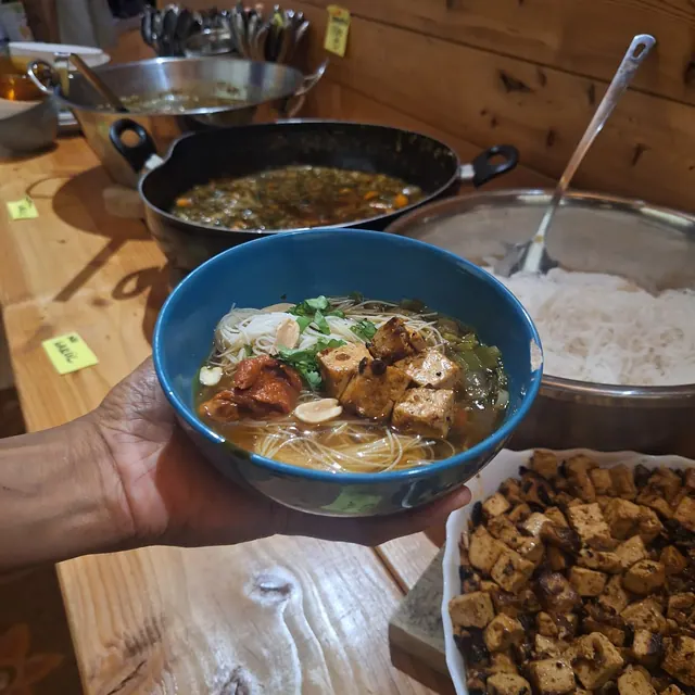 Bol de bouillon aux vermicelles de riz et tofu tenu au-dessus du buffet