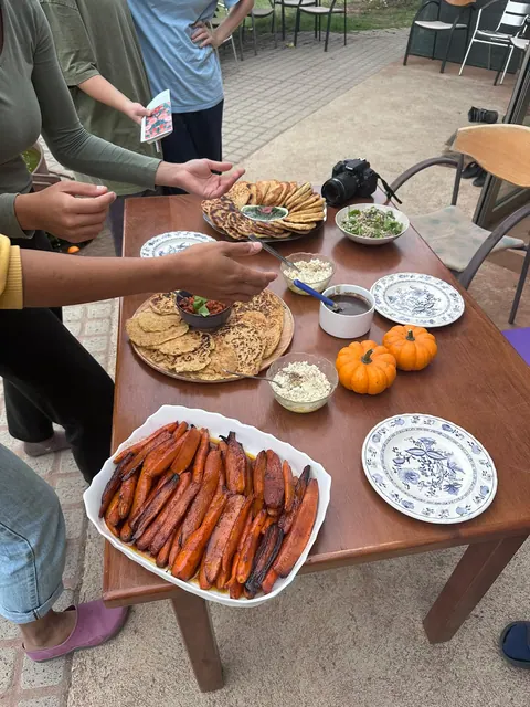 Des mains se servent sur une table : carottes rôties, petites courges, galettes, assiettes à motifs bleus
